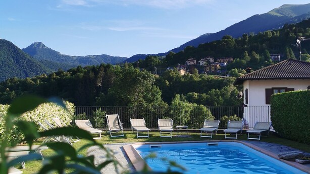 Piscina con sillas de descanso, rodeada de vegetación y montañas al fondo.