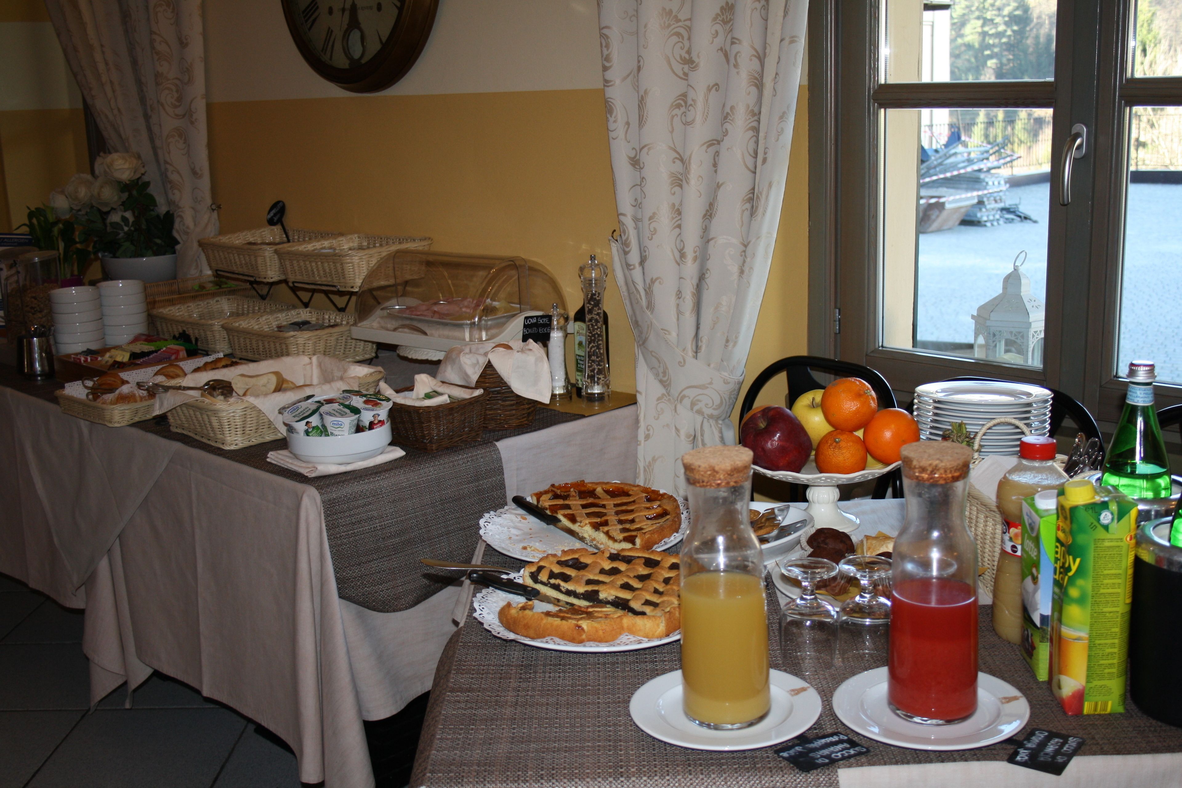 A breakfast buffet with various food items, including pastries and fruits, arranged on a table with a view of the outdoors through a window.