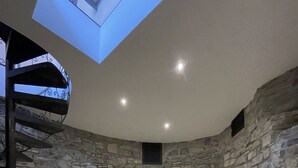 Una habitación con paredes de piedra, una escalera en espiral, un tragaluz y una ventana pequeña.