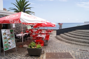 An outdoor seating area with red and white umbrellas, stone tables, and chairs.