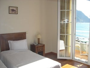 A bedroom with a bed, a nightstand, a lamp, and a view of the beach through a sliding glass door.