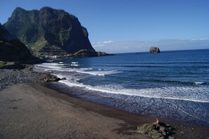 A beach with rocky terrain, a large cliff, and a small island in the distance.