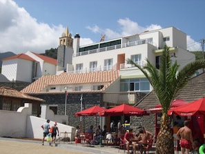 A coastal building with multiple balconies, outdoor seating, and a prominent clock tower. - Hotel Costa Linda (Machico)