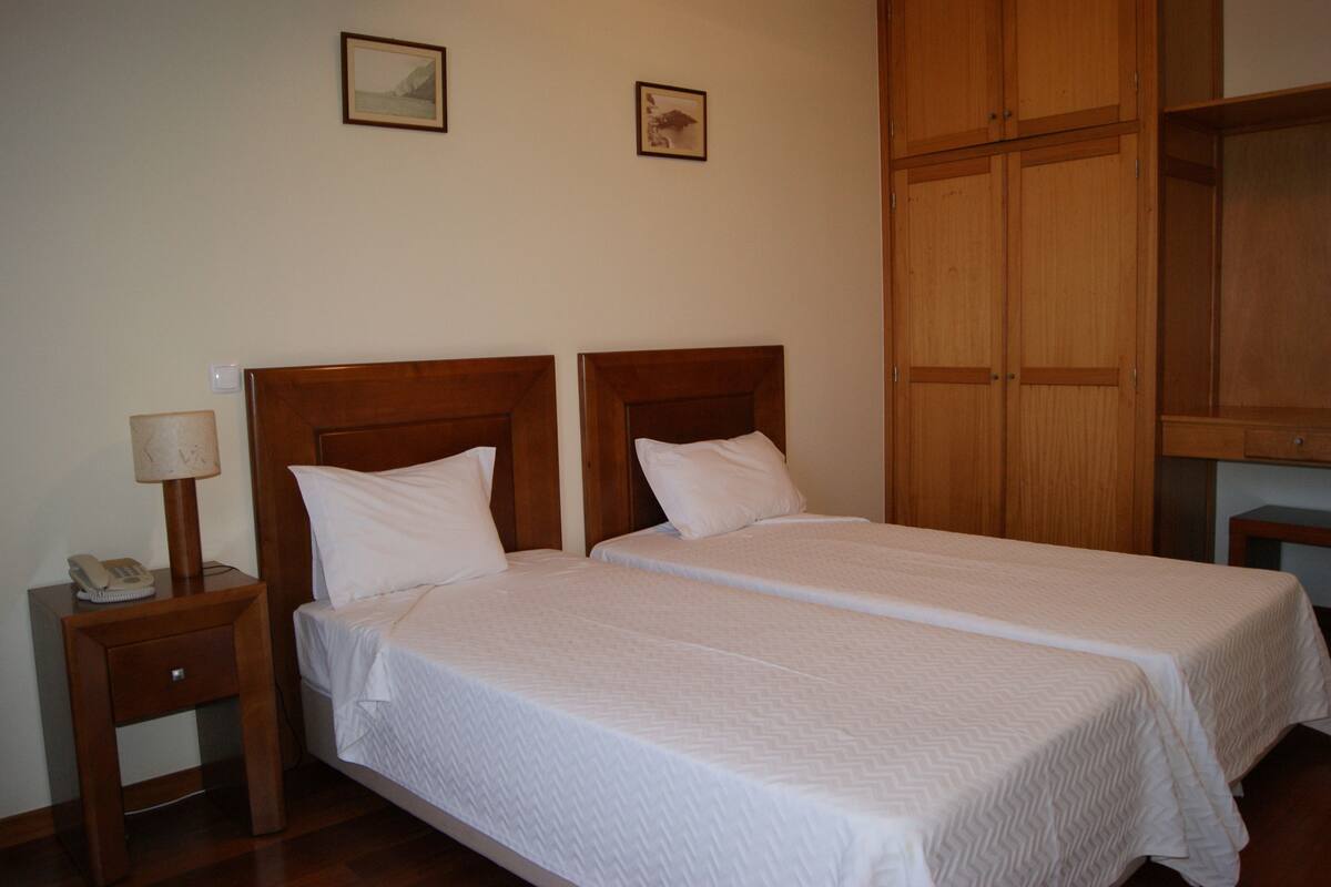 A double bed with a wooden headboard, a bedside table with a lamp, and a phone. There are two framed pictures on the wall.