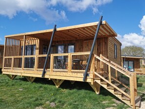 A wooden cabin with a deck, a staircase, and a covered outdoor seating area. - Le Village de Cottages - Le Pôle du Cheval et de l'Âne (La Celle-Conde)