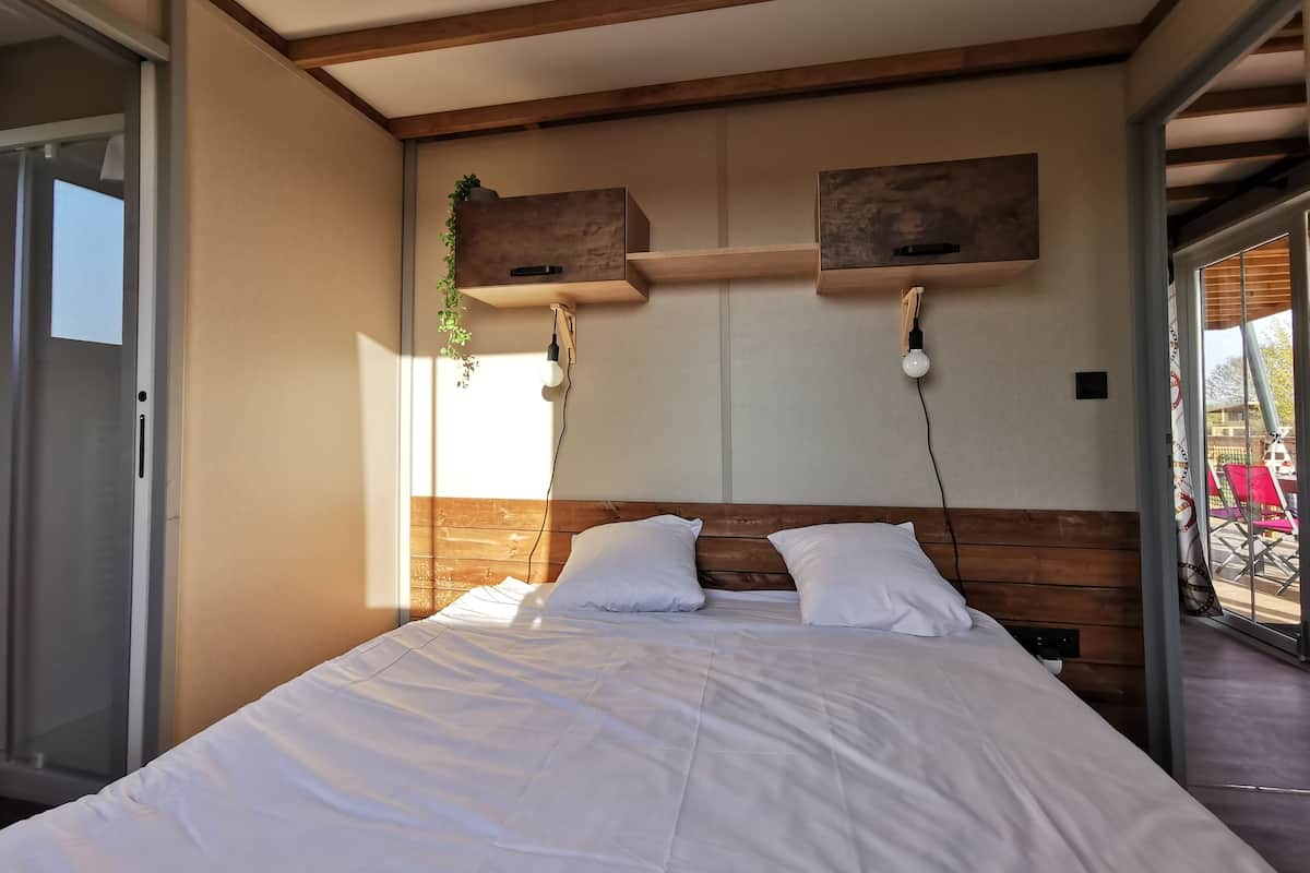 Quarto moderno com cabeceira de madeira, roupa de cama branca e prateleira embutida com uma planta.