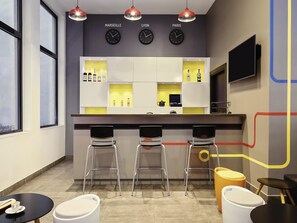 Un coin bar avec trois tabourets, un comptoir avec des bouteilles et des horloges portant les inscriptions « MARSEILLE », « LYON » et « PARIS ».