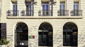 Fachada de hotel com janelas em arco, placa com o nome 'ibis Styles Hotel' e uma pequena placa verde indicando os serviços.