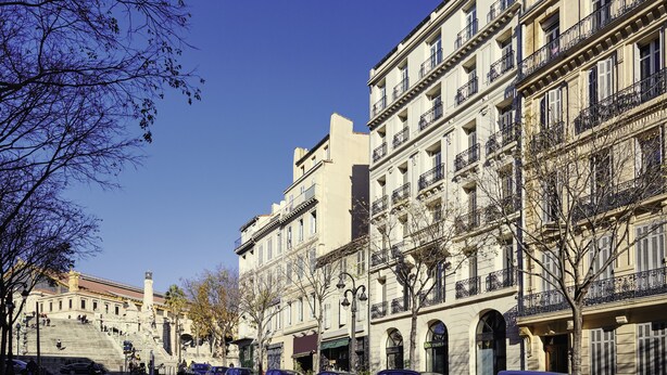 Uma fileira de edifícios clássicos em estilo europeu, com vários andares e varandas, sob um céu azul límpido.