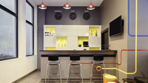 Uma área de bar moderna com três bancos, um balcão com prateleiras exibindo garrafas, e relógios com as legendas 'Marseille', 'Lyon' e 'Paris'.