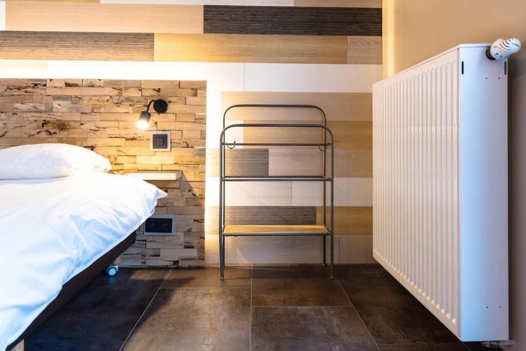 Een slaapkamer met een bed, een metalen schapunit, een wandlamp en een radiator.