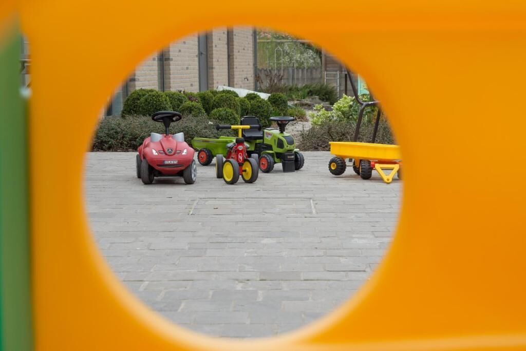 A view through a circular frame of three toy tractors and a yellow toy wagon parked on a paved surface.