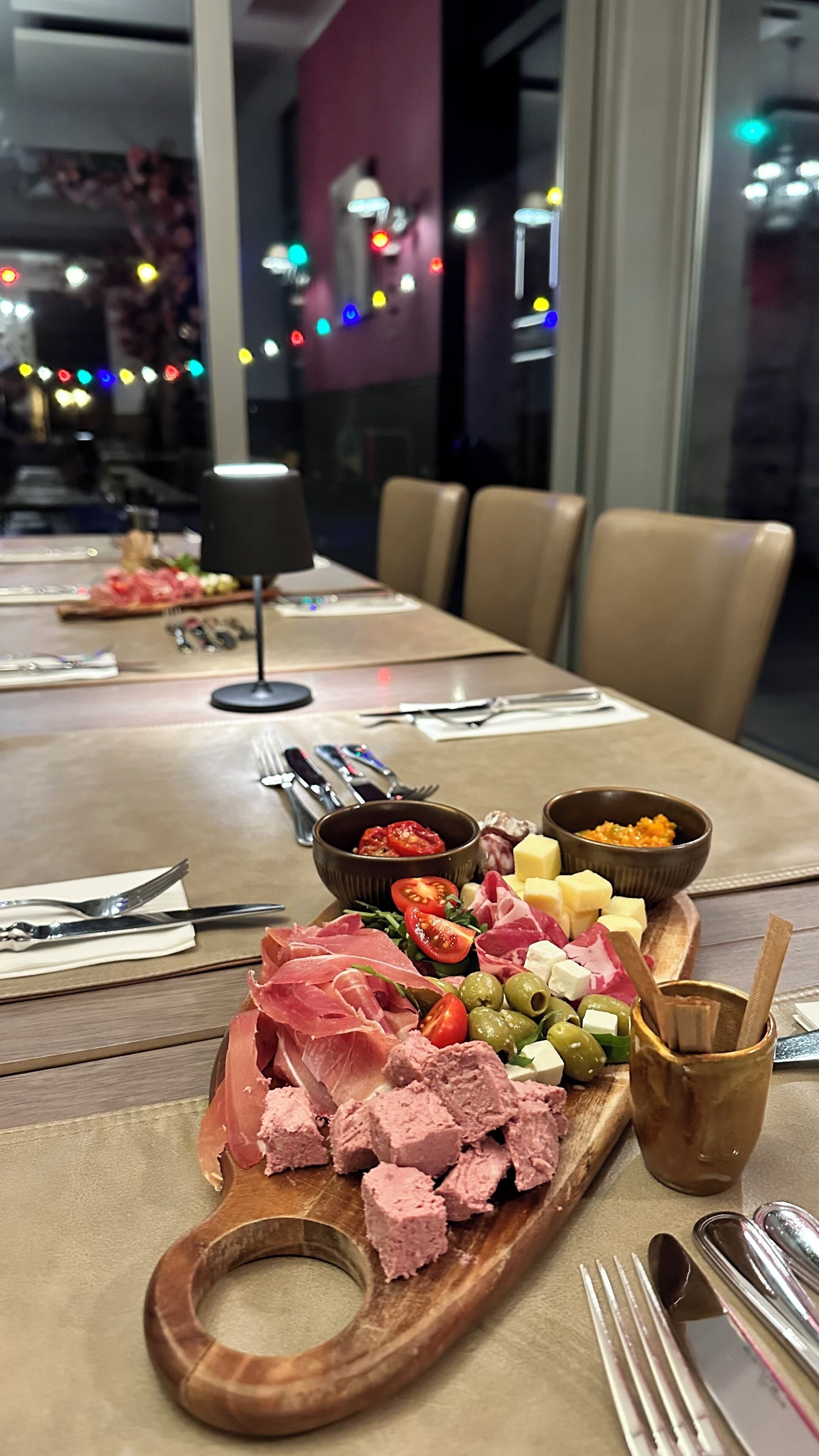 Een eettafel met diverse soorten eten, zoals vleeswaren, kazen en olijven, gepresenteerd op een houten plank.