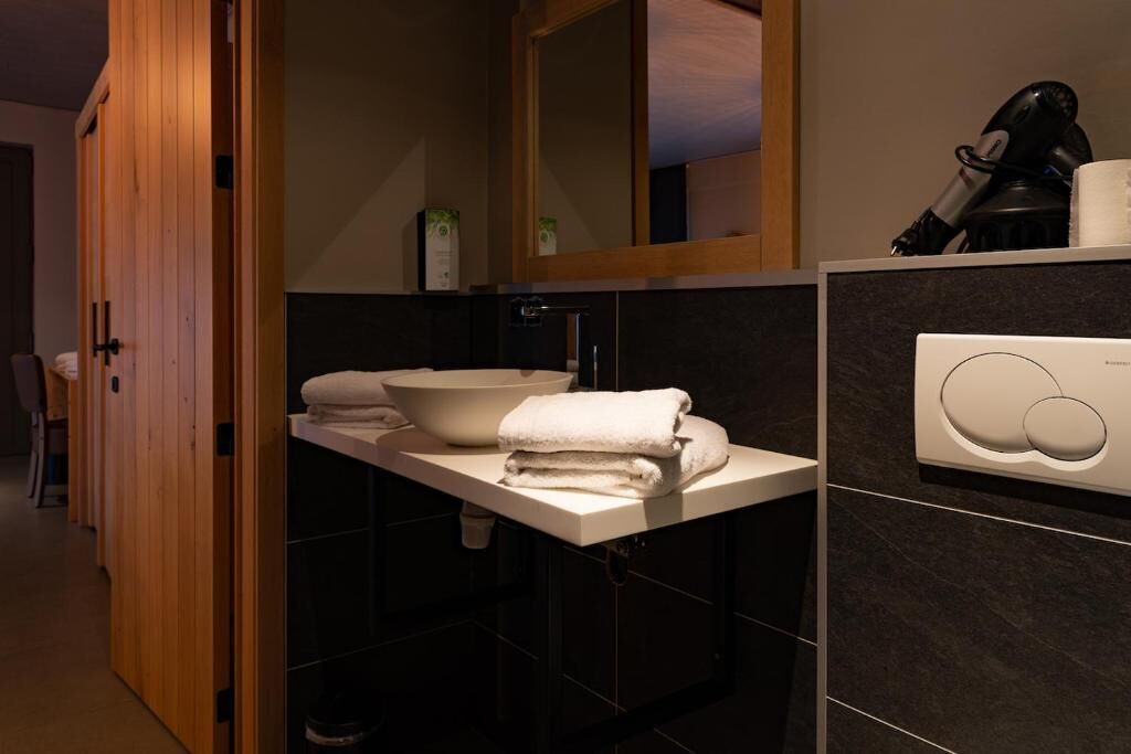Une salle de bain moderne avec une porte en bois, un lavabo blanc, un grand miroir et un porte-serviettes.