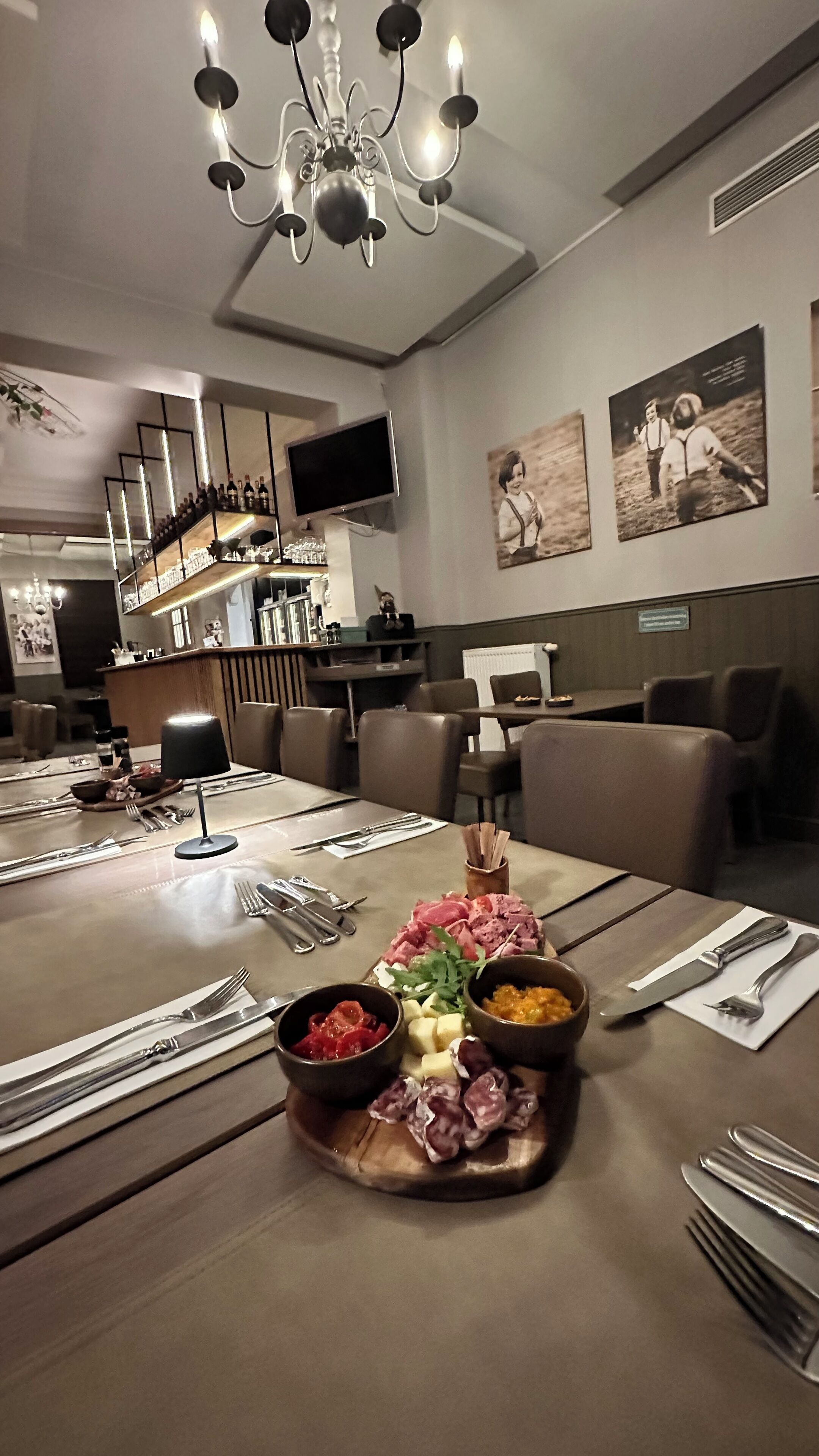 Ein Essbereich mit einem Holztisch, gedeckt für eine Mahlzeit, inklusive einer Platte mit verschiedenen Fleisch- und Käsesorten, und einer darüber hängenden Chandelier.