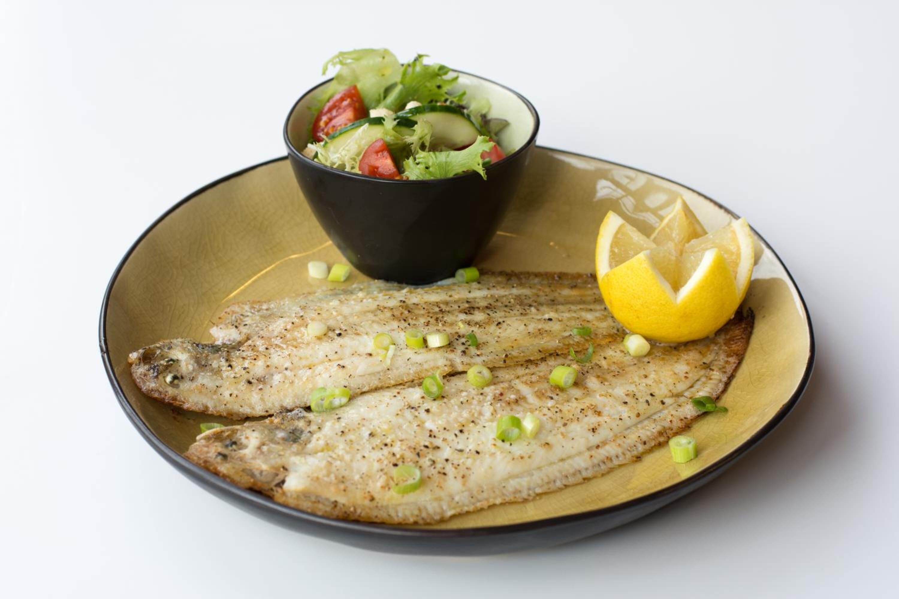 A plate with two fish fillets, a bowl of salad, and a lemon wedge.