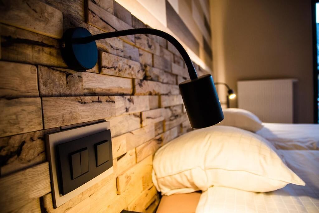Un lit avec une literie blanche et une tête de lit en bois agrémentée d’un luminaire au design moderne.