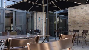 An outdoor seating area with tables and chairs, a large umbrella, and a brick wall. - 't Oud gemeentehuis Poelkapelle (Langemark-Poelkapelle)