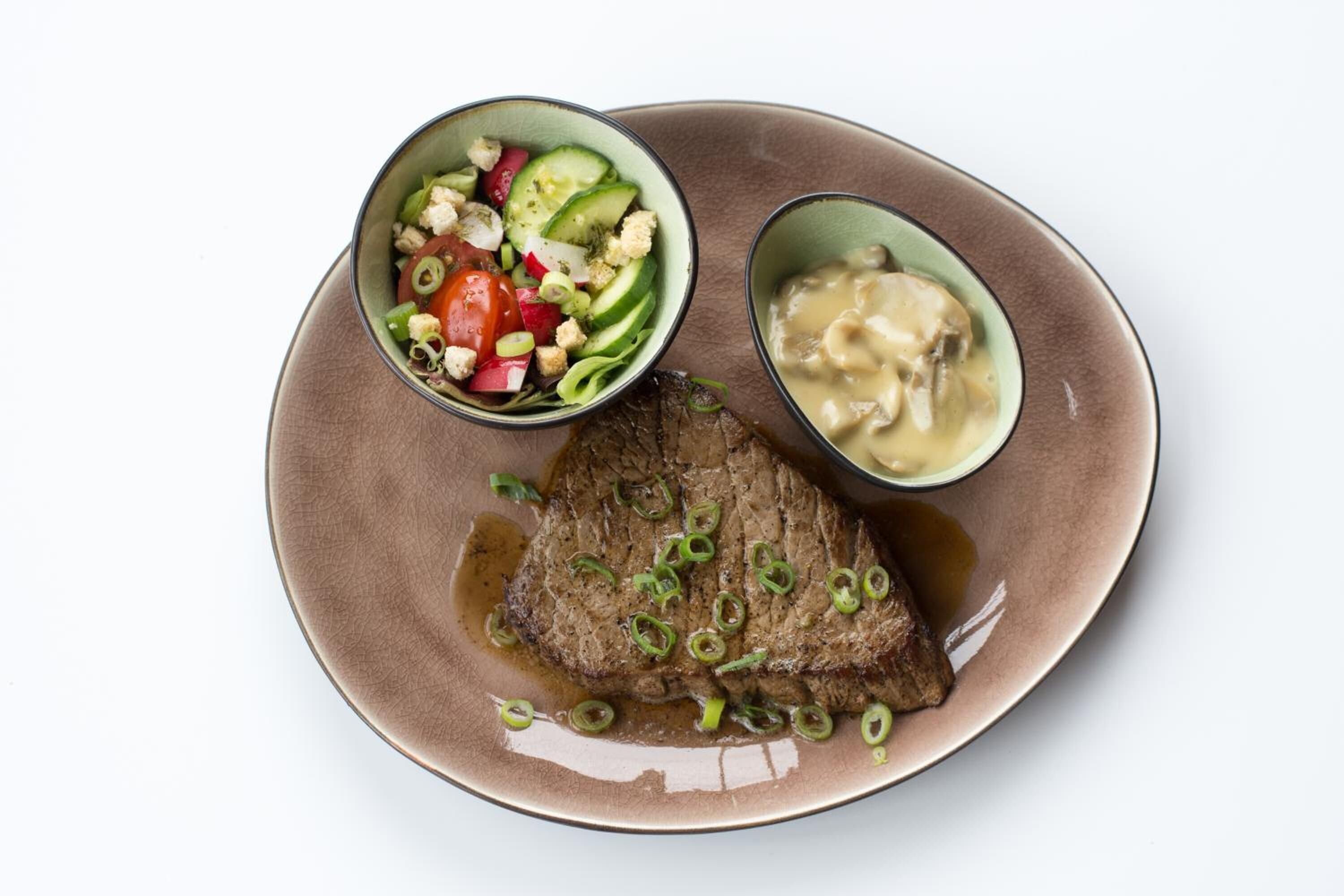 A plate with a steak, a salad, and a creamy sauce.