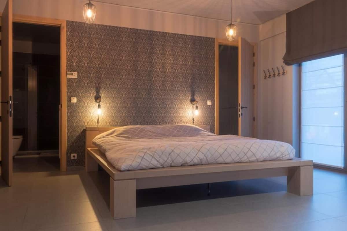 Une chambre moderne avec un lit, deux lampes fixées au mur, un papier peint à motifs et une grande fenêtre.