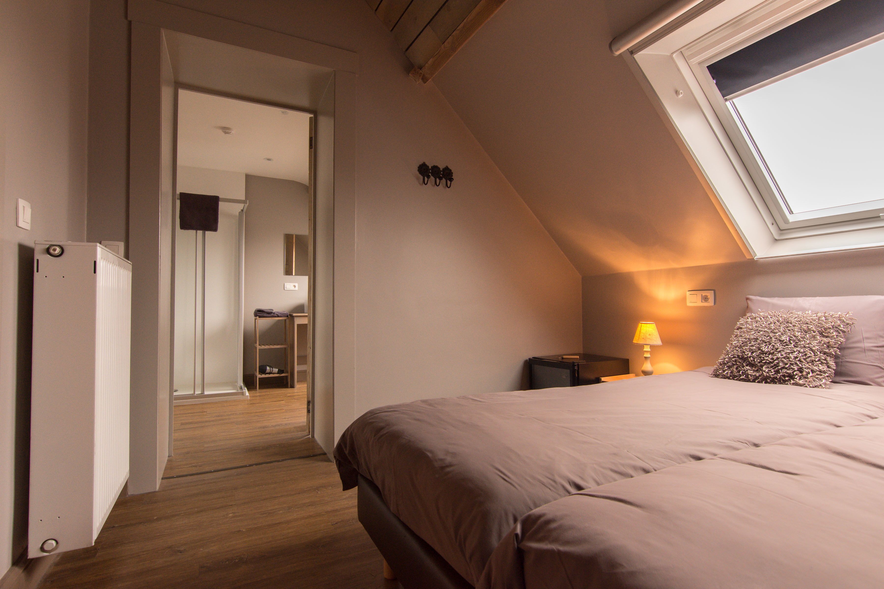 A bedroom with a sloped ceiling, a bed with a headboard, a nightstand with a lamp, and a window.