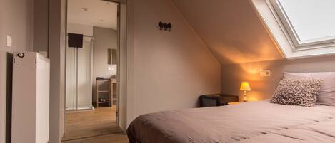 A bedroom with a sloped ceiling, a bed with a headboard, a nightstand with a lamp, and a window.