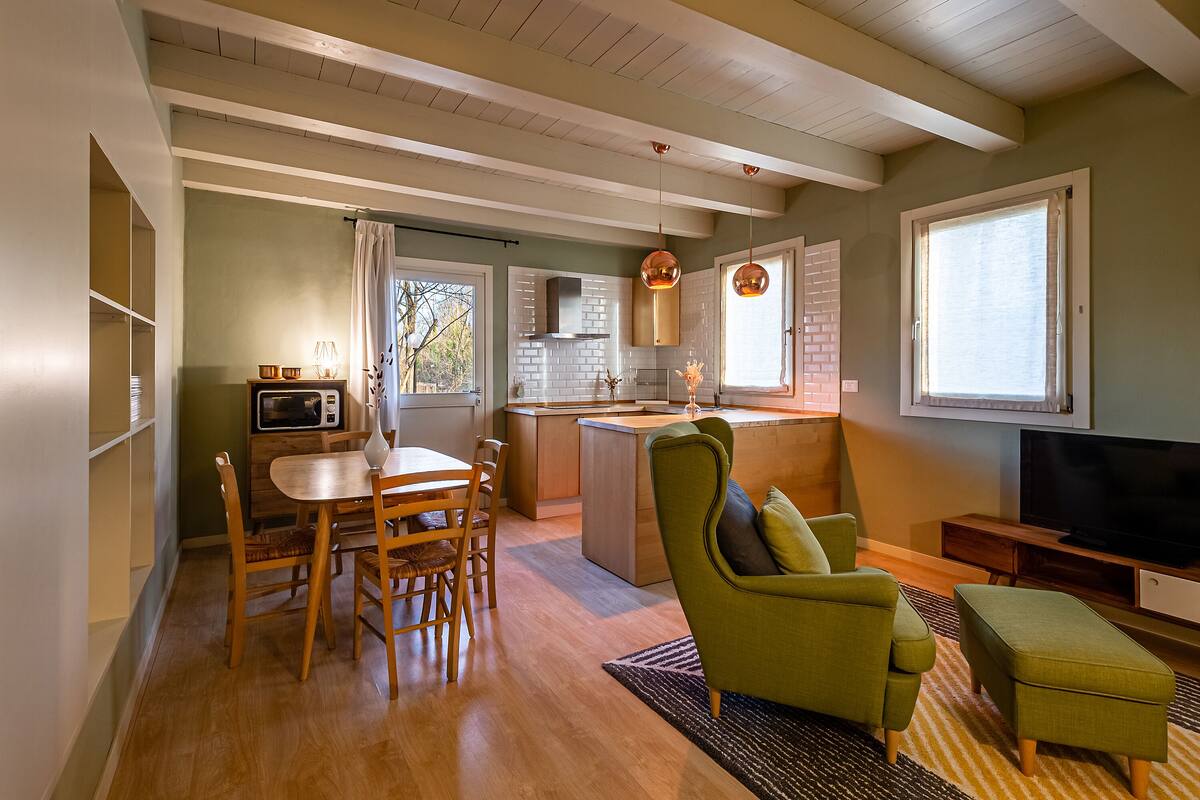 Una cocina moderna con zona de comedor, un sillón verde y una televisión.