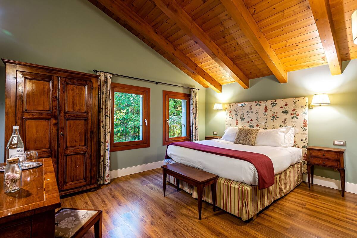 Un dormitorio con techo de madera, una cama grande con cabecera floral, dos lámparas de noche y un armario de madera.