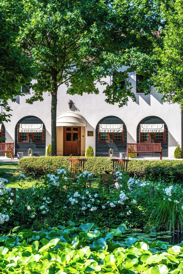 A building with arched windows, a wooden door, and a bench in the garden.