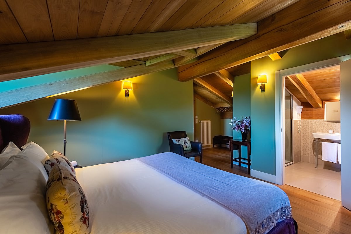 Un dormitorio con una cama, un escritorio, una silla y un baño visible a través de una puerta abierta.