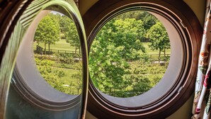 Blick durch ein Fenster mit Holzrahmen auf eine grüne Landschaft mit Bäumen und einem Zaun.