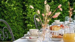 Ein Tisch gedeckt mit Teetassen, einer Vase mit getrockneten Blumen, einer Teekanne und einem Brot.