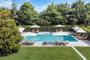 A swimming pool with lounge chairs and umbrellas, surrounded by greenery.