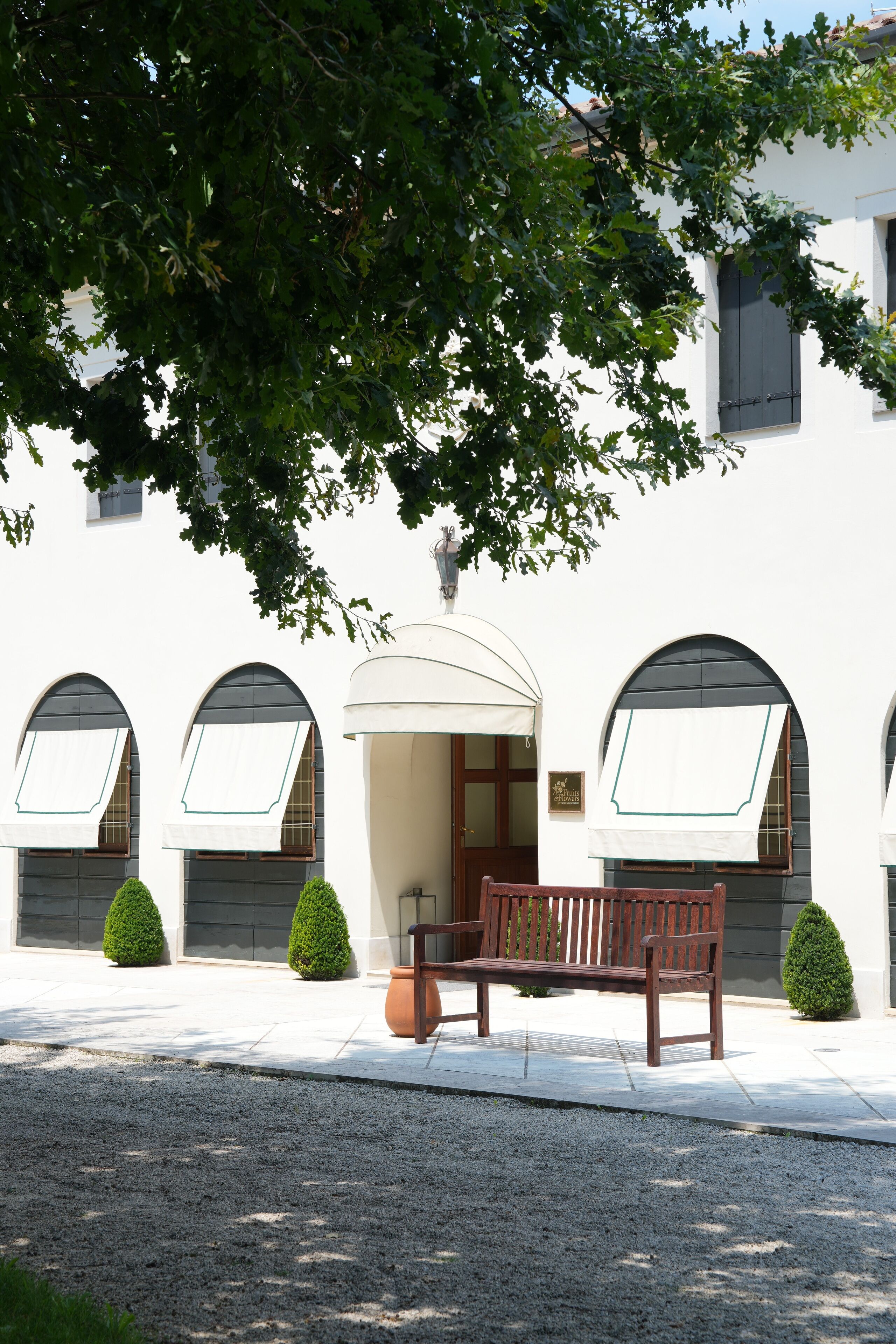 A building with arched windows, a bench, and a tree in front.
