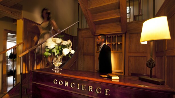 Ein Empfangstresen mit einer Namensschild, auf der 'CONCIERGE' steht, und einer Vase mit weißen Blumen.
