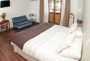 A hotel room with a large bed, a blue sofa, a small table with a lamp, and a TV mounted on the wall.