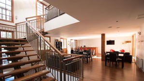 A spacious living area with a wooden staircase, a dining area with a table and chairs, and a kitchen in the background. - Hotel Loreto (Santiago)