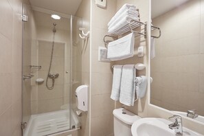 A modern bathroom with a glass-enclosed shower, a toilet, a sink, and a towel rack with neatly folded towels. - Hotel Loreto (Santiago)