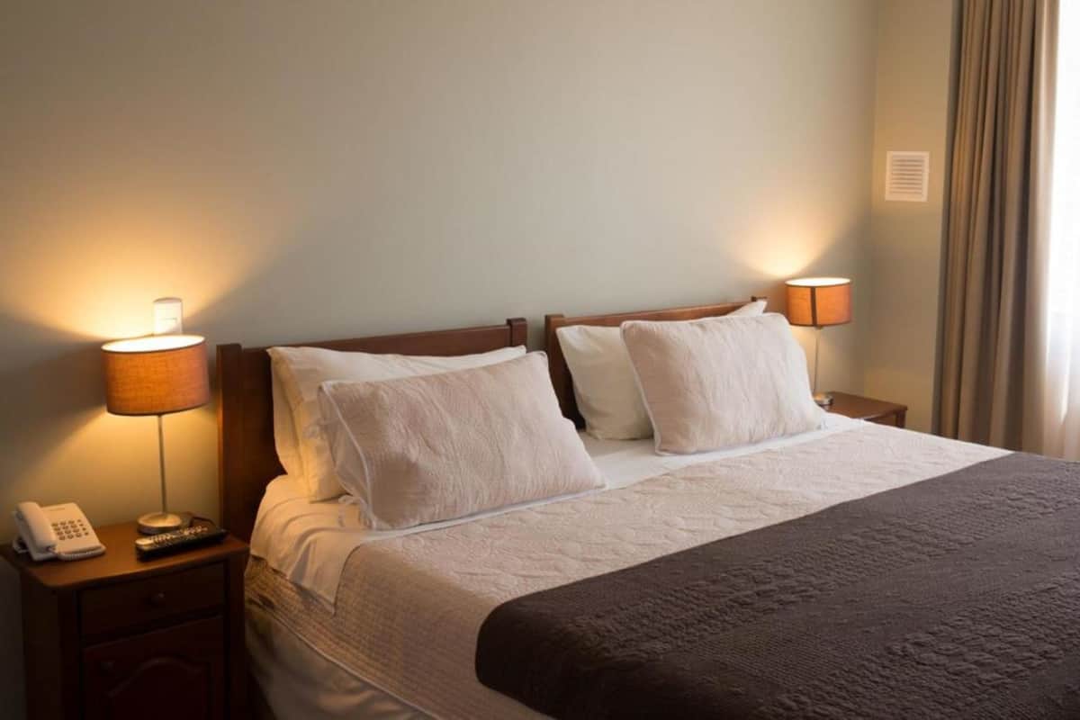 A hotel room with a large bed, two bedside lamps, a telephone, and a small table.