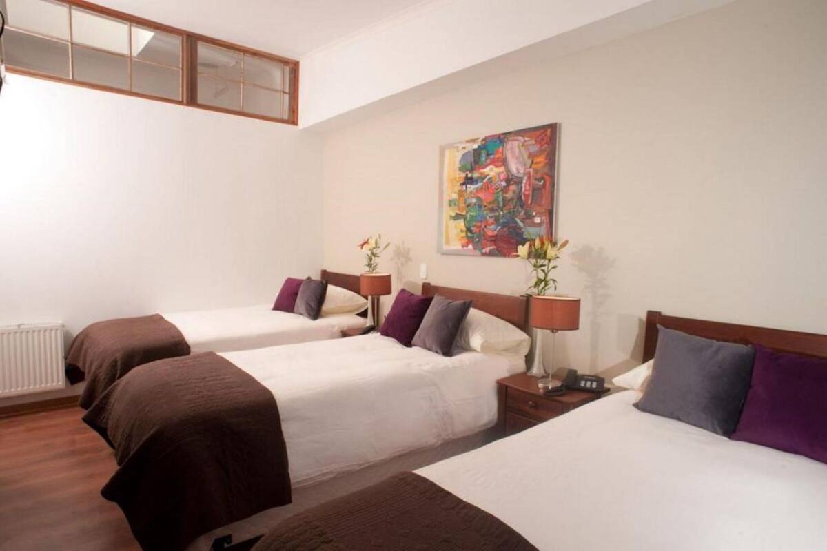 A hotel room with two beds, each with a nightstand, a lamp, and a painting on the wall.