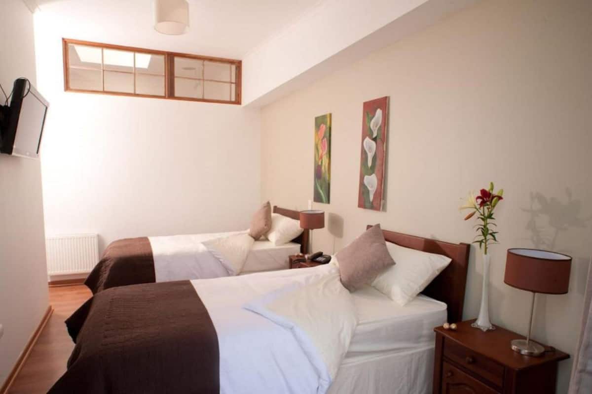 A hotel room with two beds, a bedside table with a lamp, a nightstand, and artwork on the wall.