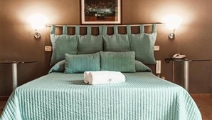 A neatly made bed with a green bedspread and pillows, a white towel, and a framed picture on the wall. - Hotel La Palma (Catania)