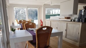 A dining area with a white table, wicker chairs, and a view of the outdoors through large windows. - Maison Kerkhove (Avelgem)