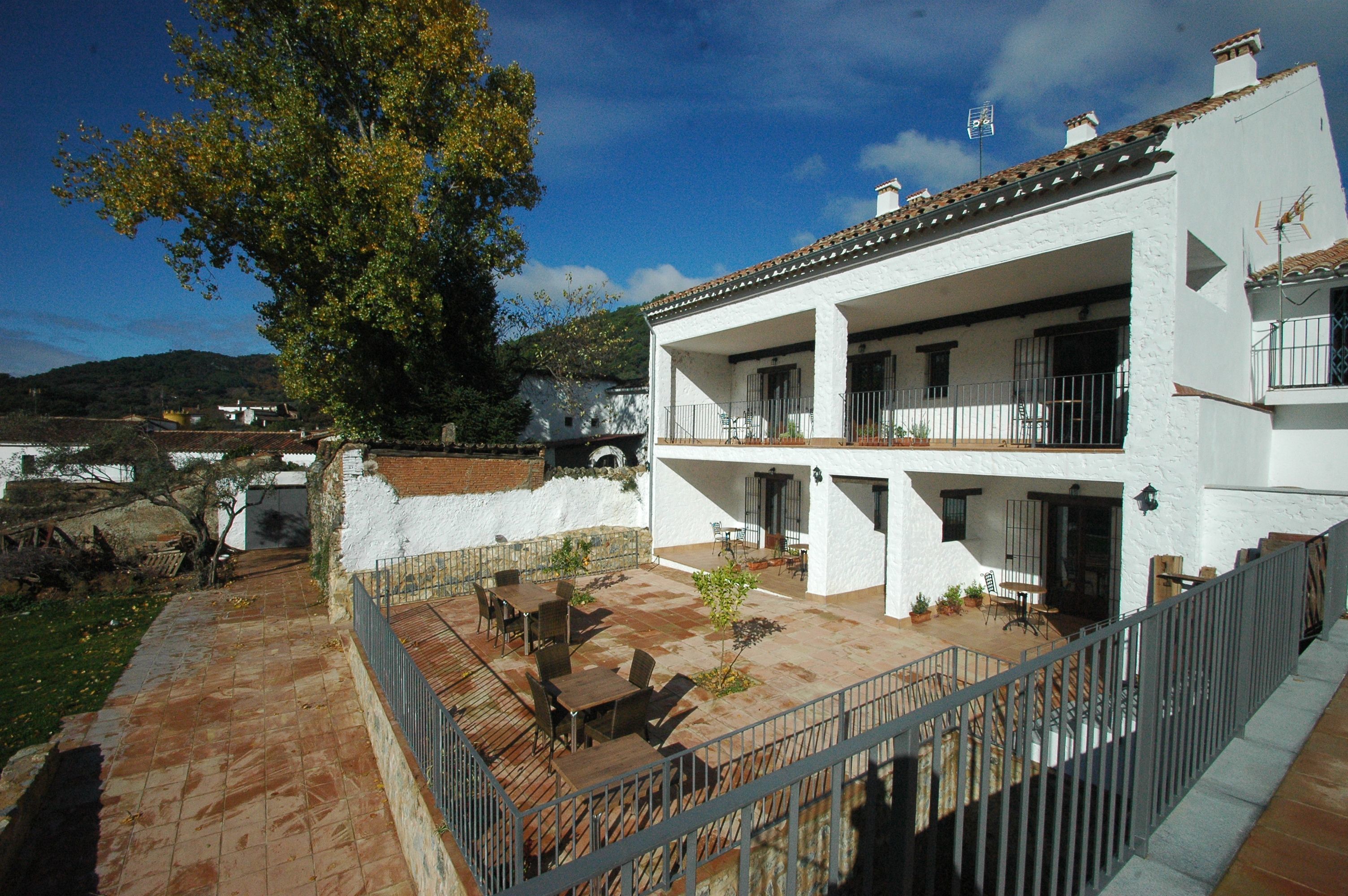 A two-story white building with a tiled roof, a balcony, and a patio area with outdoor furniture.