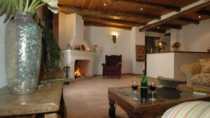 A cozy living room with a fireplace, a red armchair, a wooden coffee table with a wine bottle and glass, and a striped sofa. - La Posada de San Marcos (Alajar)