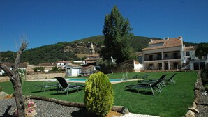 A hotel with a pool, lounge chairs, and a view of a hill. - La Posada de San Marcos (Alajar)