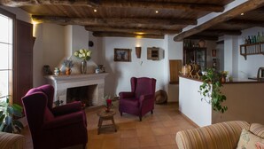 A cozy living room with a fireplace, two armchairs, a striped sofa, and a kitchen area with shelves of bottles and a potted plant. - La Posada de San Marcos (Alajar)