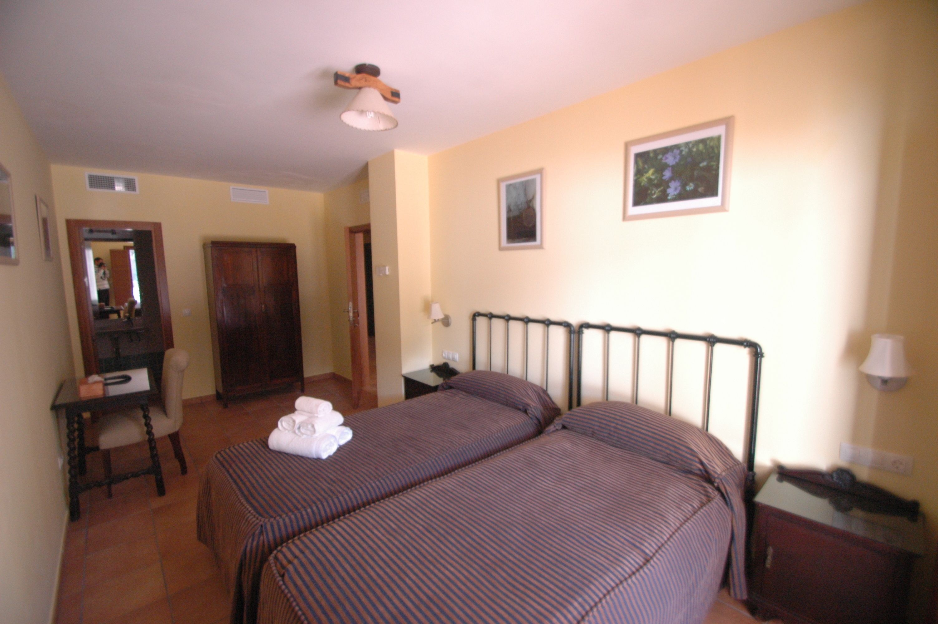 A hotel room with two beds, a desk, a chair, a wardrobe, and a bathroom.