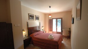 A bedroom with a large bed, a bedside table, a nightstand, a lamp, a chair, and a window with curtains. - La Posada de San Marcos (Alajar)