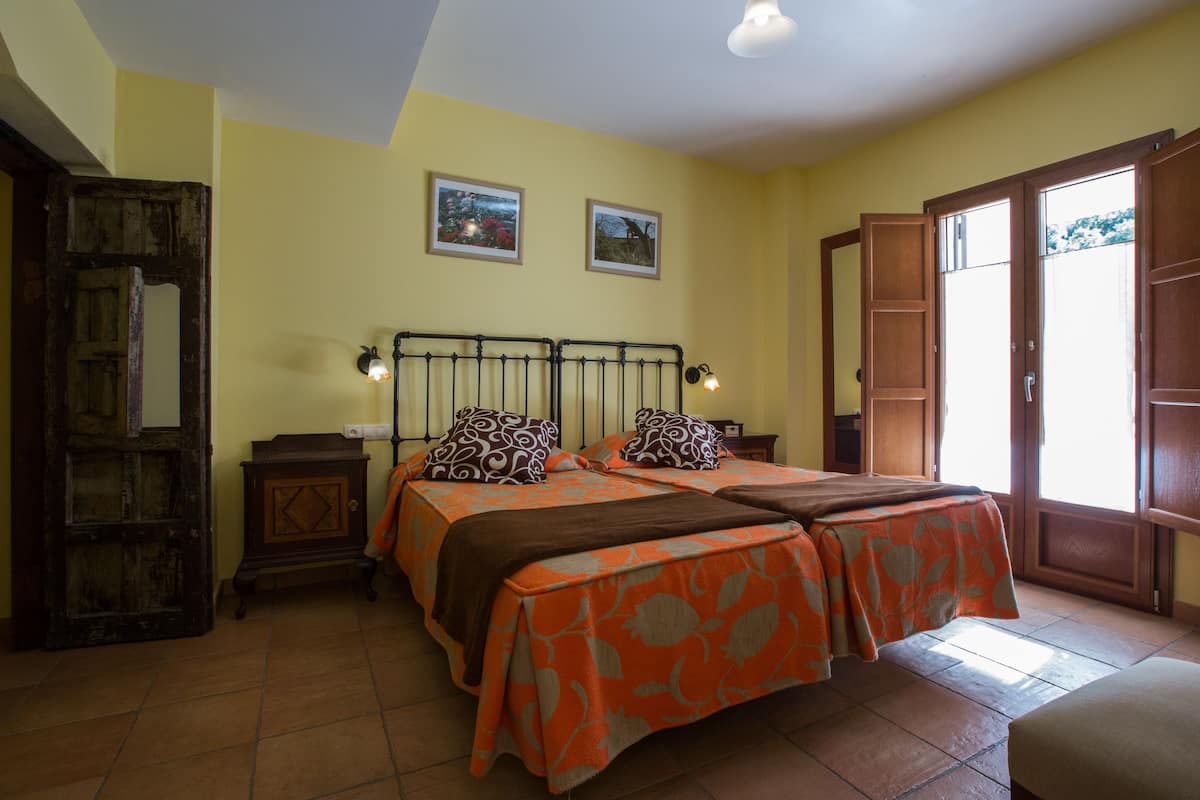 A bedroom with two beds, a wooden door, a small cabinet, and two wall-mounted lamps.